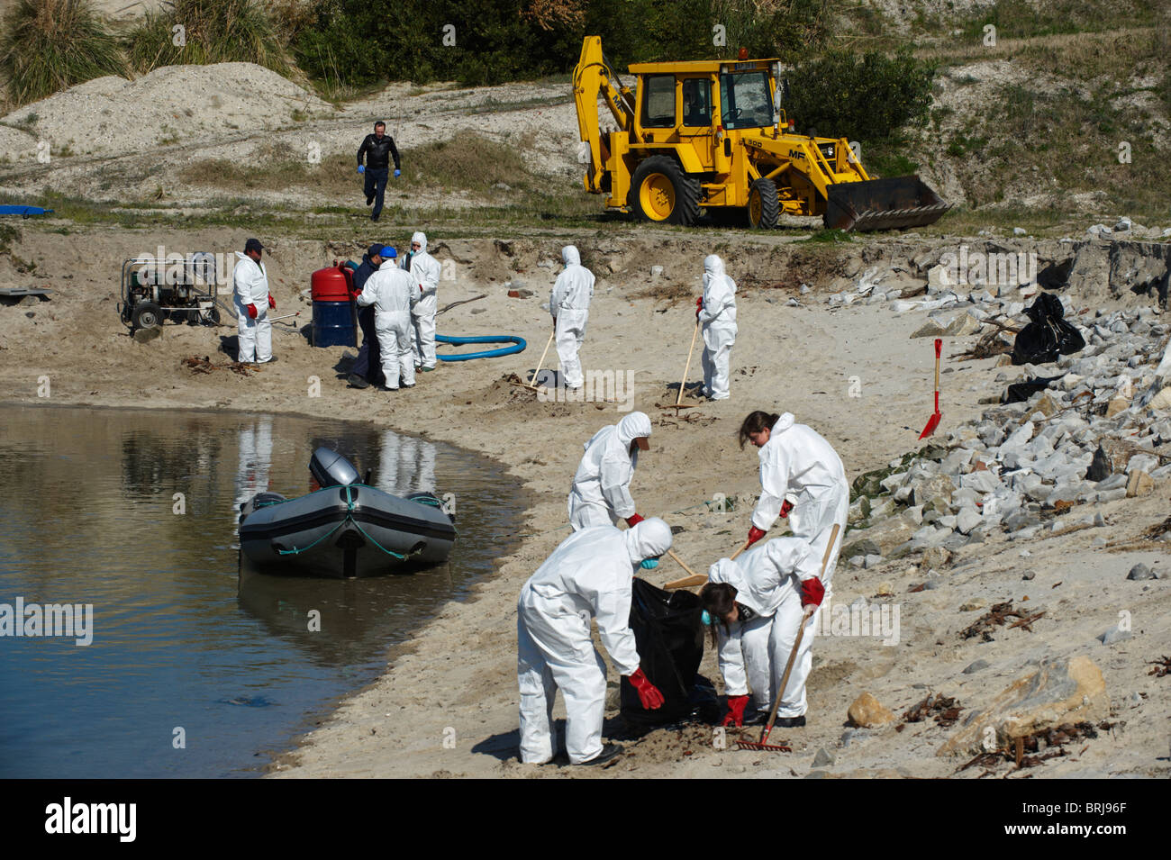 Männer in Ganzkörper-schützende Kleidung und Atemschutzmasken reinigen einen Strand Stockfoto