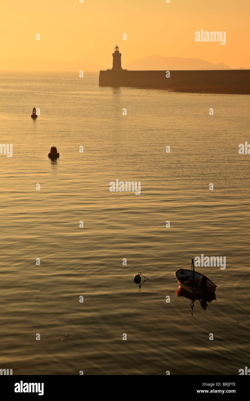 Vor Sonnenaufgang leuchtet St Peter Port Leuchtturm in Guernsey mit der Insel Herm Silhouette am Horizont Stockfoto