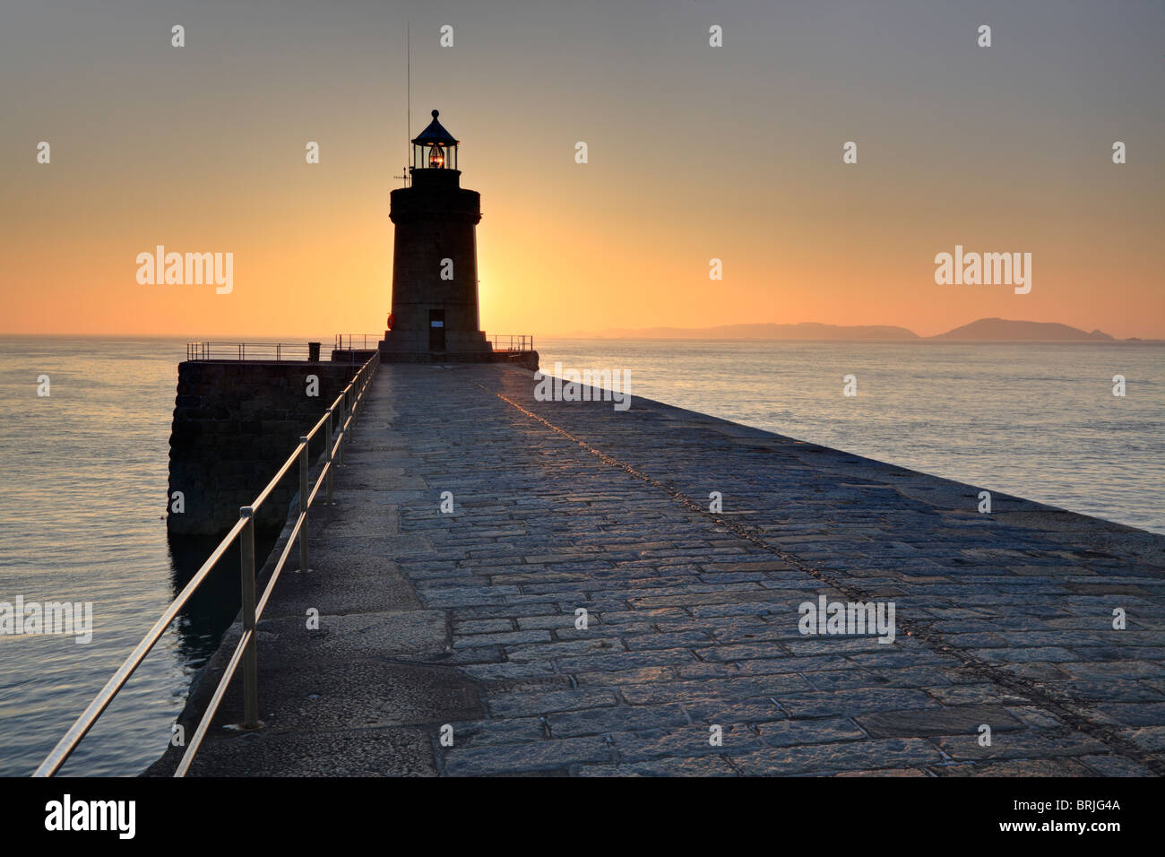Sunrise leuchtet St Peter Port Leuchtturm in Guernsey mit der Insel Herm Silhouette am Horizont Stockfoto