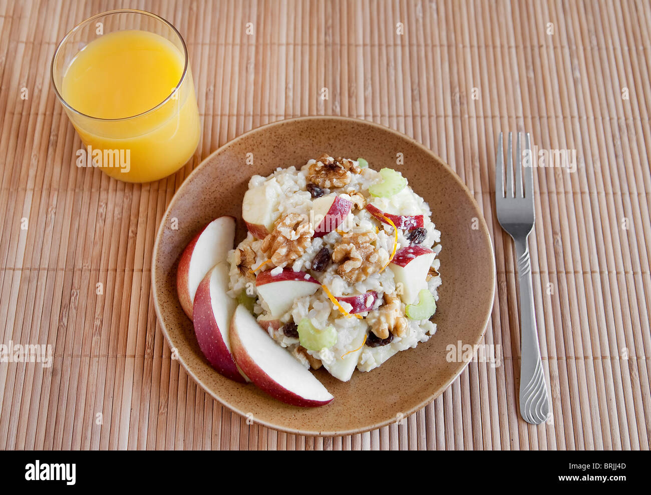 ein Teller mit Apfel Walnuss Salat ähnlich Waldorf-Salat auf einem braunen Teller mit Glas Orangensaft Stockfoto