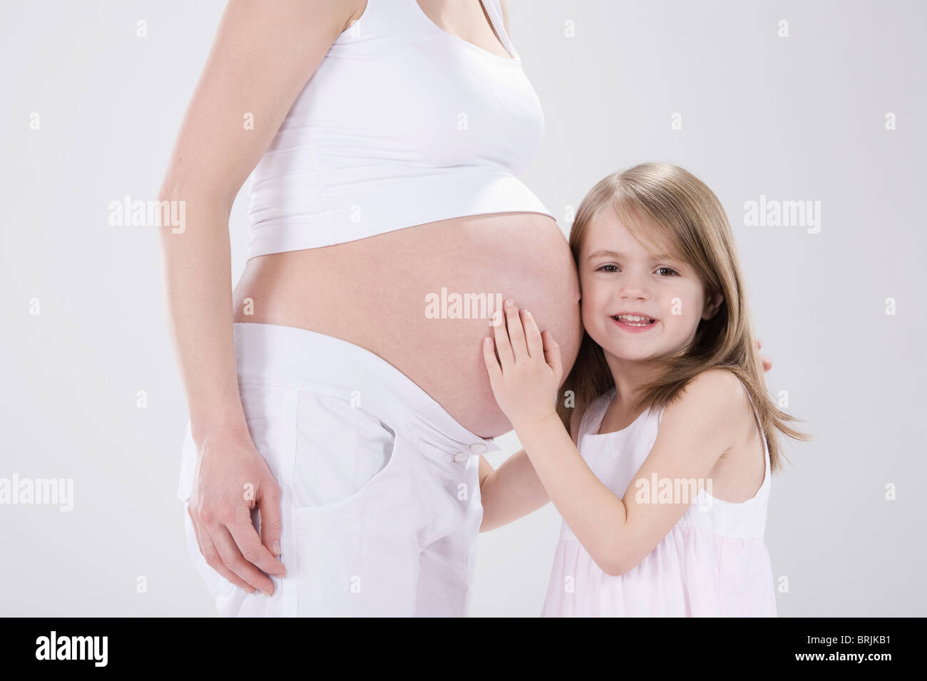 Kleine Mädchen umarmt schwangere Mutter Stockfoto