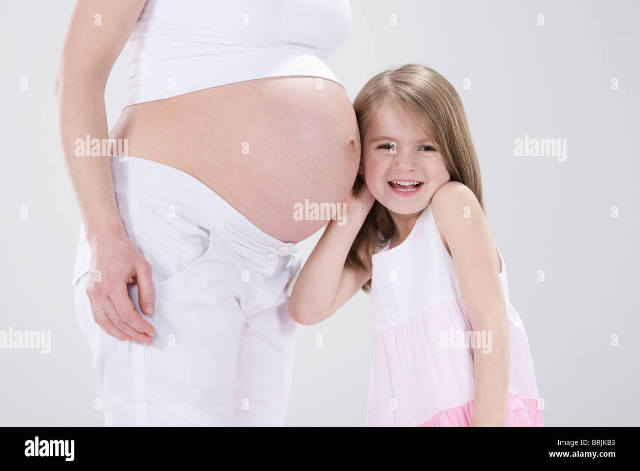 Kleine Mädchen umarmt schwangere Mutter Stockfoto