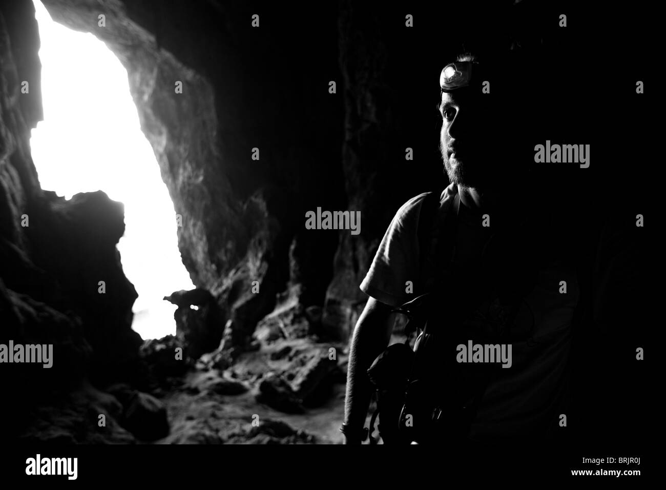 Bärtiger Mann erforscht eine Tropfsteinhöhle mit seiner Stirnlampe. Stockfoto