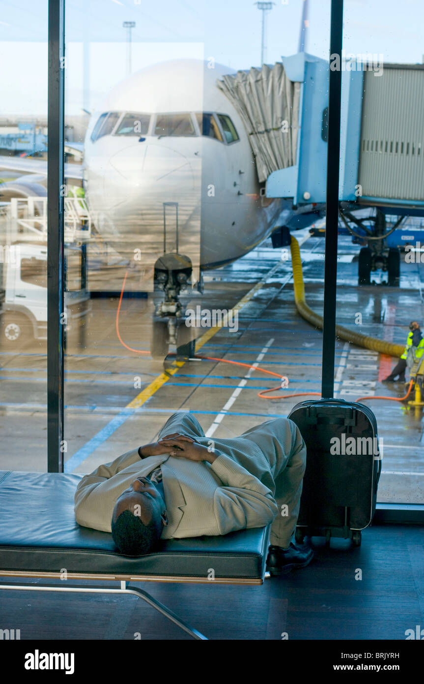 Mann schlafen im Flughafen-Terminal aufgrund von Verzögerungen, Flugzeuge im Hintergrund Stockfoto