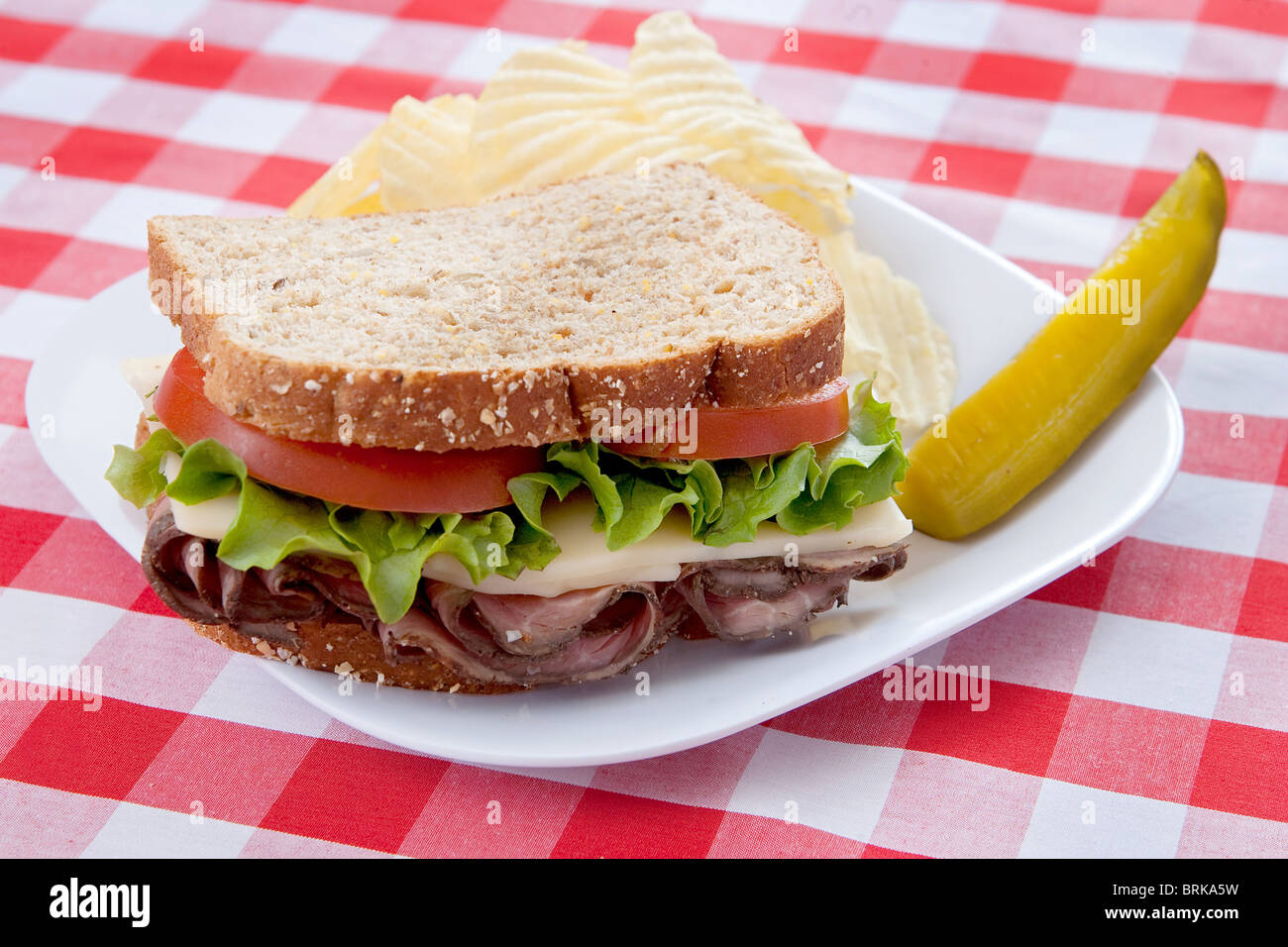 eine große roast Beef Sandwich auf Hafer-Brot mit Tomaten und Salat auf einem Teller mit klassischen rot-weiß karierte Tischdecke Stockfoto