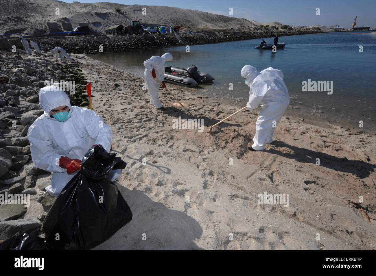 Männer in Ganzkörper-schützende Kleidung und Atemschutzmasken reinigen einen Strand Stockfoto
