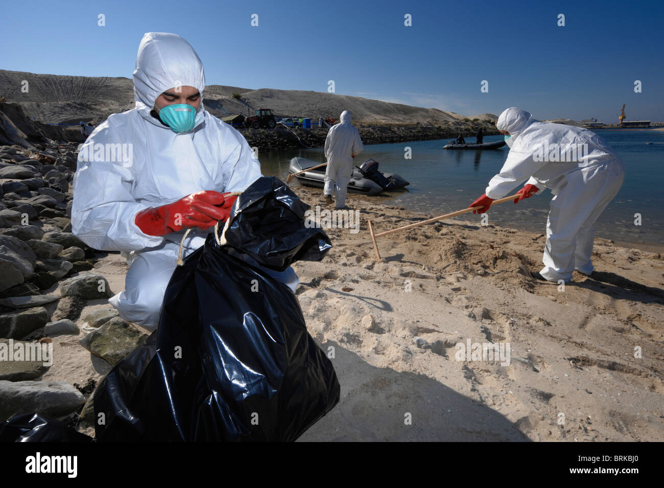 Männer in Ganzkörper-schützende Kleidung und Atemschutzmasken reinigen einen Strand Stockfoto