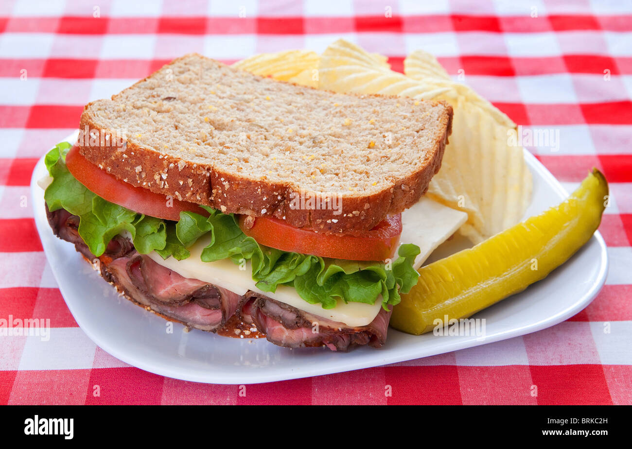 gebratenes Rindfleisch und Käse-Sandwich mit Salat, Tomate und Gurke auf einen klassischen rot-weiß karierten Hintergrund Stockfoto