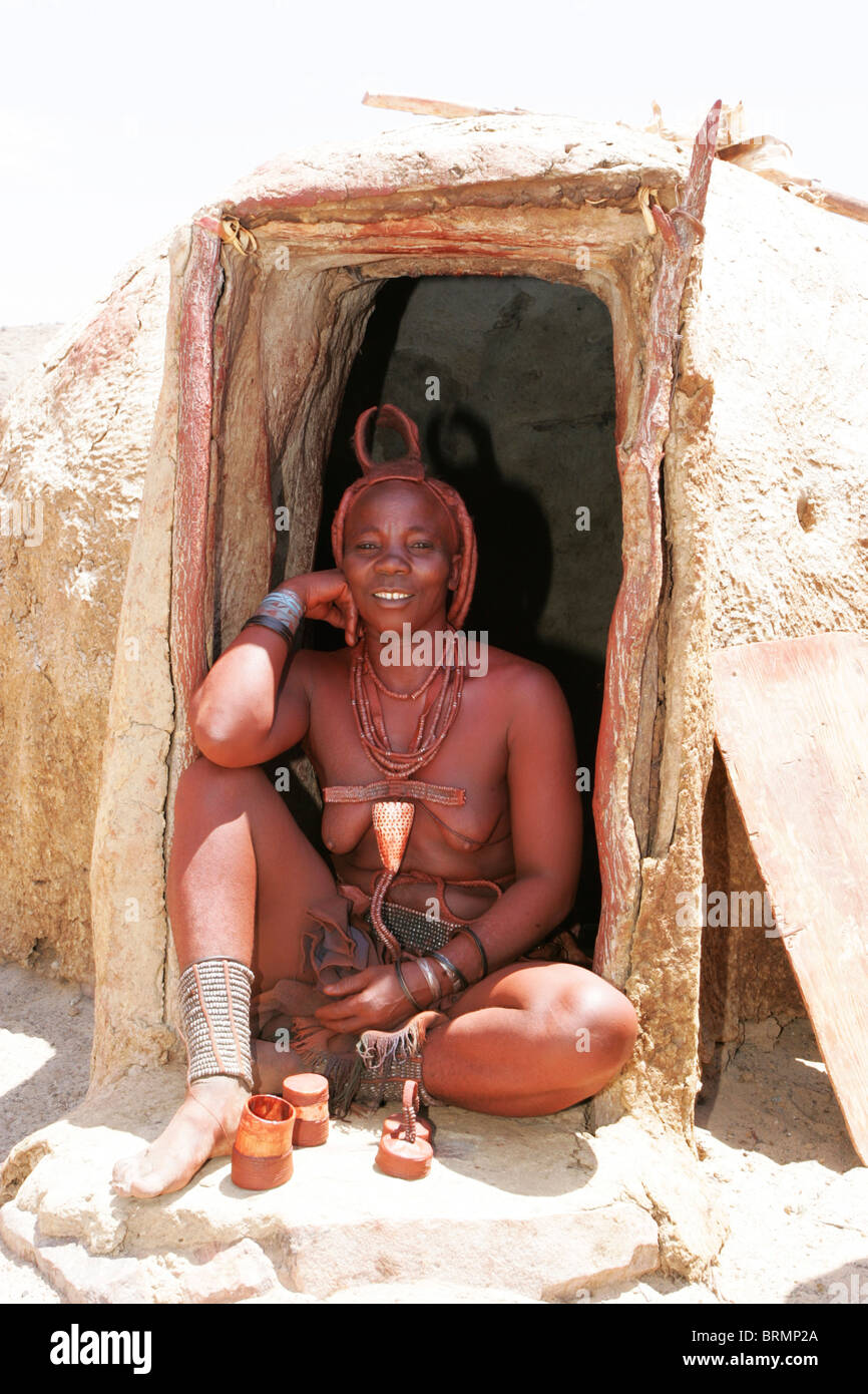 Himba Frau sitzt am Eingang ihrer Hütte Stockfoto