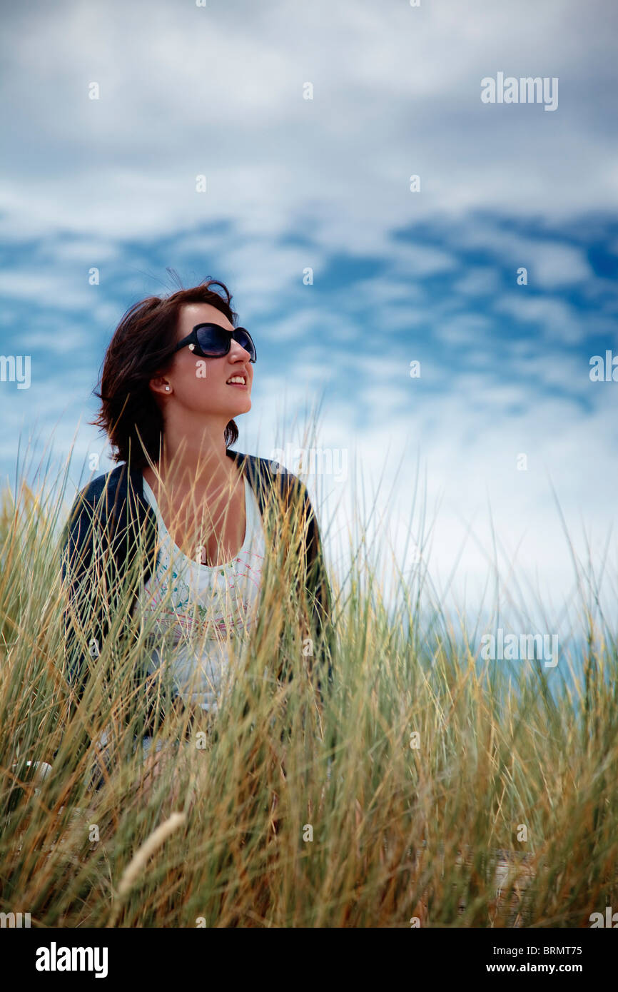 Frau mit Sonnenbrille sitzen in langen Rasen schaut zum Himmel empor Stockfoto