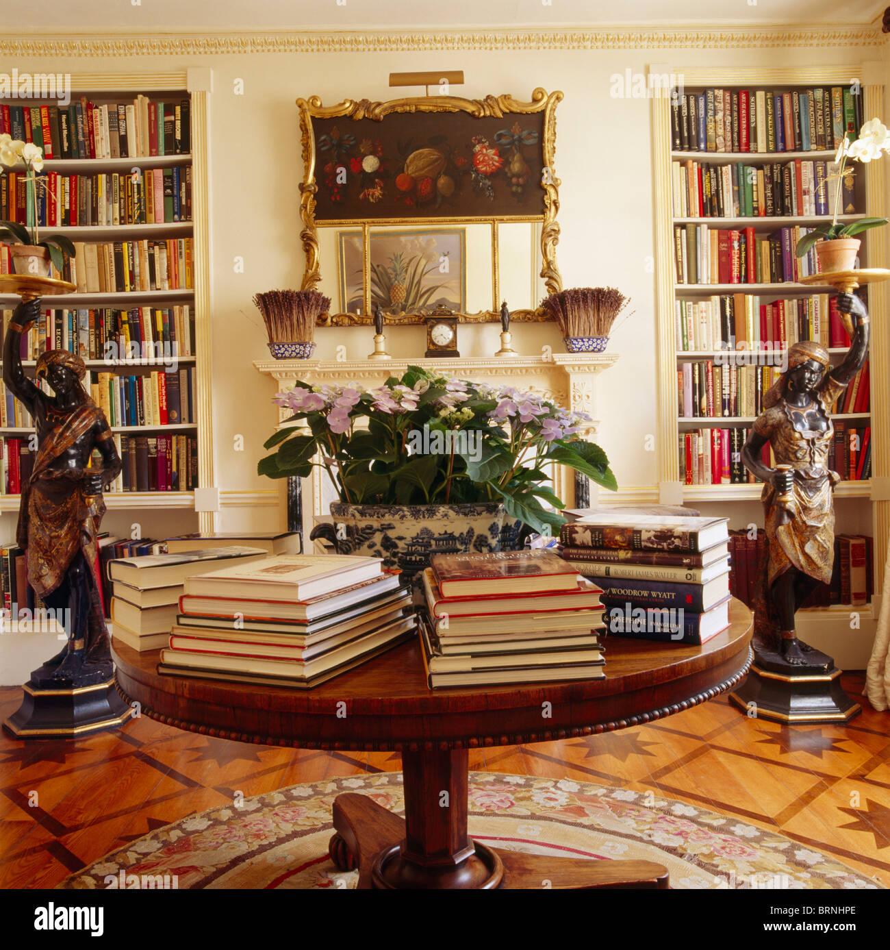 Bücher in den Stapel auf kreisförmigen antiker Tisch im Speisesaal Bibliothek mit Bücherregalen und Schaubudenbesitzers Boden bis zur Decke Statuen Stockfoto