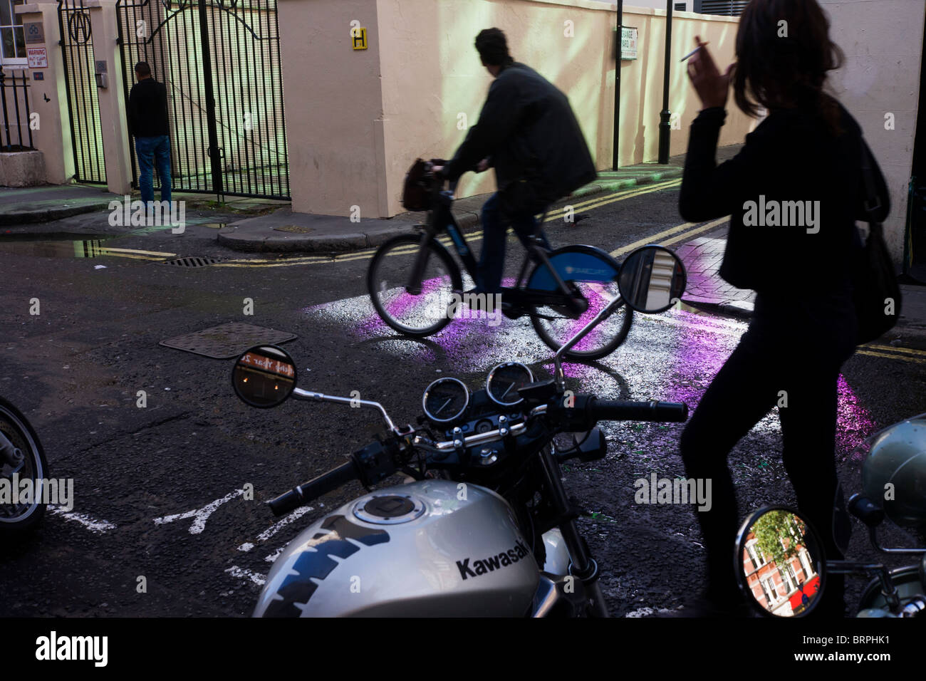 Fußgänger und Radfahrer auf Vermietung Boris Bike in einer Seitenstraße Soho pattened mit lila. Stockfoto