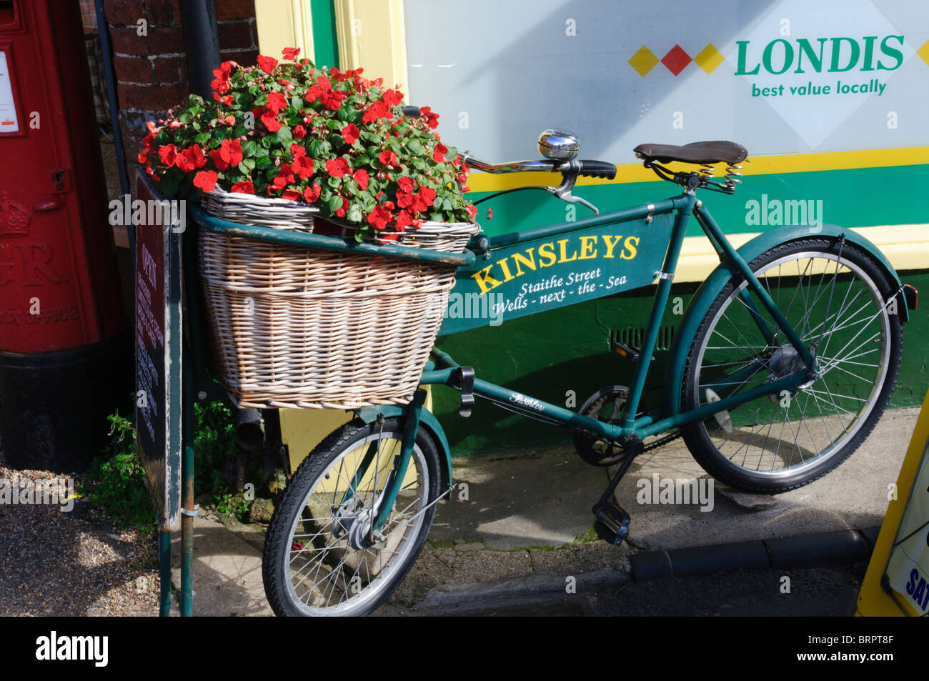 Dekorative Blumen im Weidenkorb von einem alten Tradebike als Werbung vor einem Geschäft Stockfoto