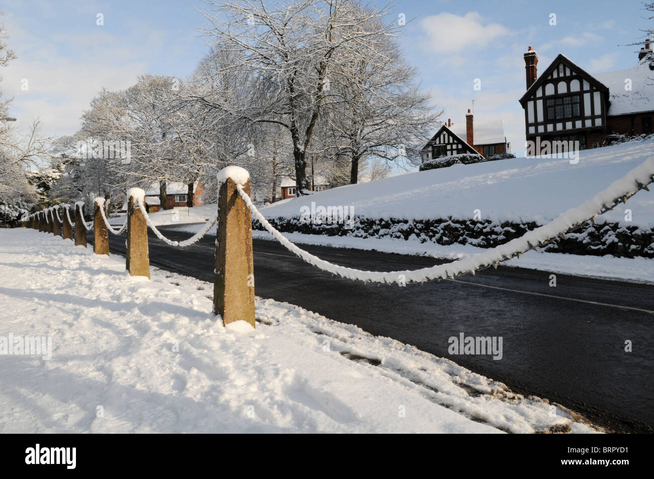 Schneebedeckte Fahrbahn und Kette Geländer mit schwarzen und weißen Fachwerkhäusern und blauer Himmel in Tettenhall, Wolverhampton Stockfoto