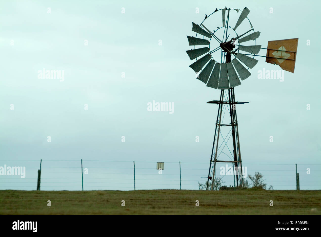 Eine alte ramponierte Windmühle steht neben einem Bauernhof Zaun Stockfoto