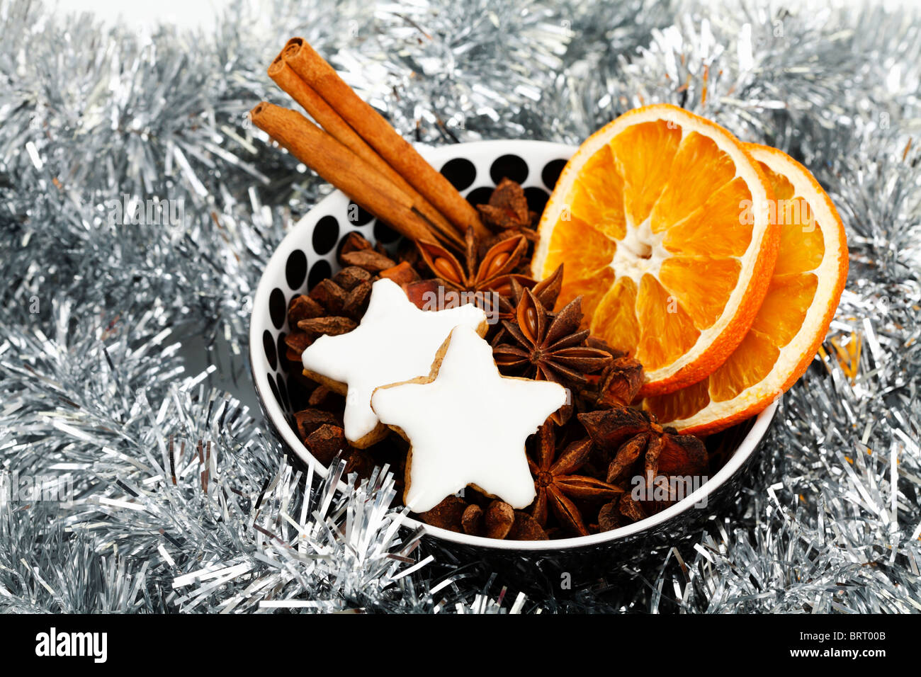 Sternförmige Zimt Kekse mit getrockneten Scheiben Orange, Zimtstangen und Anis Sterne in einer Schüssel mit Weihnachtsschmuck Stockfoto