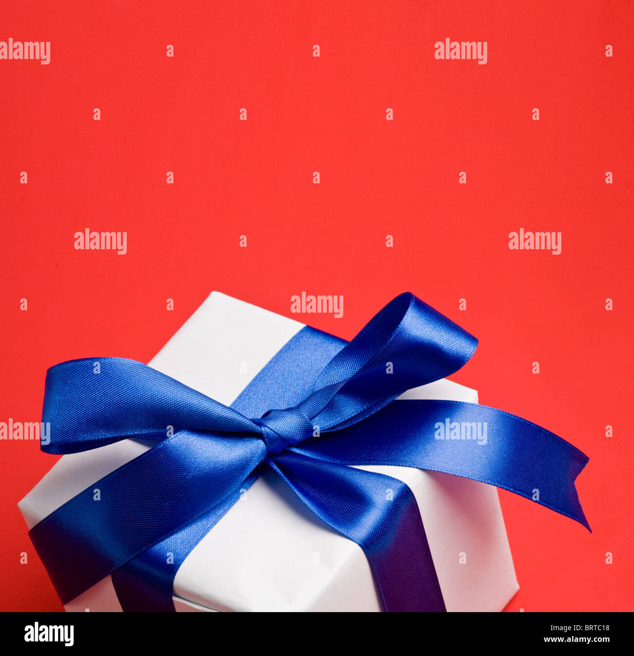 weiße Geschenk mit einem blauen Band auf rotem Grund Stockfoto
