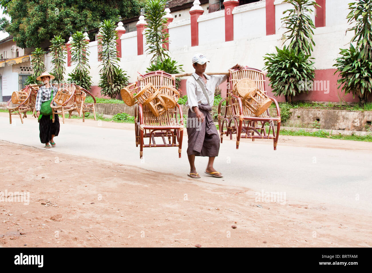 Zwei Burmesen mit handgefertigten Möbeln vorbei an einer Tempelwand in Chiang Tong, Myanmar Stockfoto