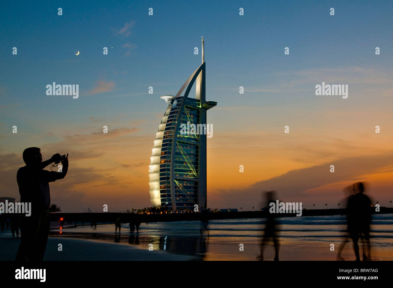 Menschen am Strand vor das Luxus-Hotel Burj al-Arab bei Sonnenuntergang, Dubai, Vereinigte Arabische Emirate Stockfoto