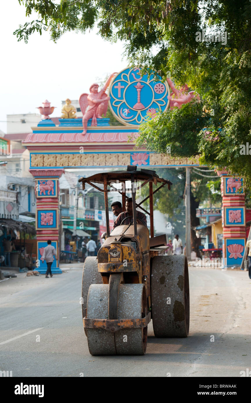 Indische Dampfwalze mit einem dekorativen Beton Sarva Dharma Symbol Torbogen, der die Straße im Hintergrund umfasst. Puttaparthi, Andhra Pradesh, Indien Stockfoto