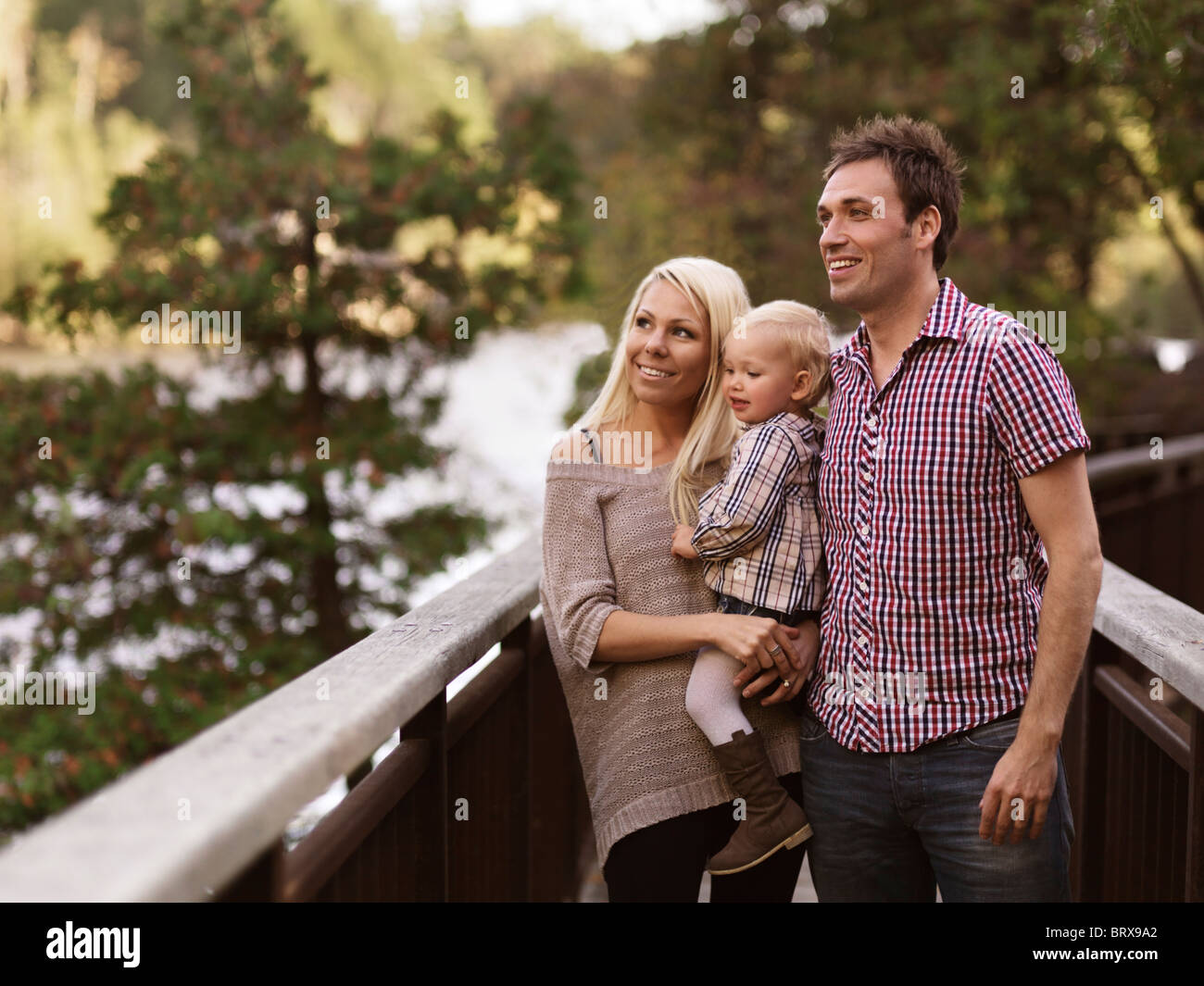 Führerschein erhältlich unter MaximImages.com - glückliche, lächelnde junge Eltern und ein zweijähriges Mädchen, das den Blick auf die Natur von einer Brücke aus genießt. Ontario, Kanada. Stockfoto