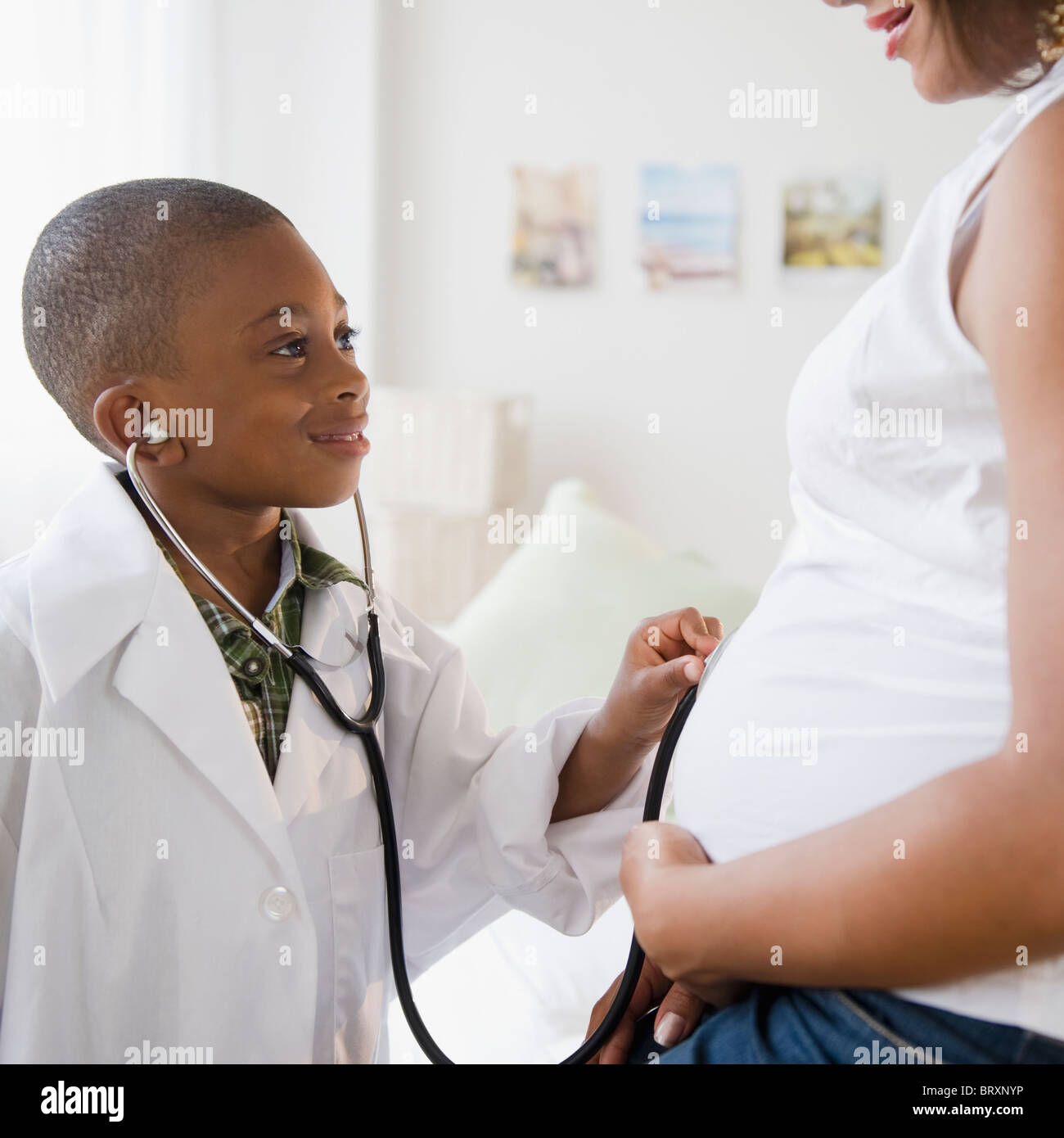 Schwarzer Junge in Kittel, Stethoskop, schwangere Mutter Bauch halten Stockfoto