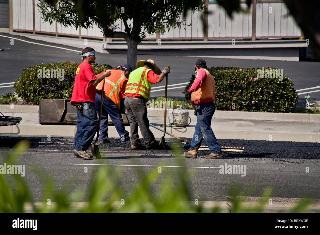 Hispanische Arbeiter tragen Hochsicht Sicherheitswesten verteilt heiße Gülle auf Fahrbahn auf einer Straße in Laguna Niguel, CA Stockfoto