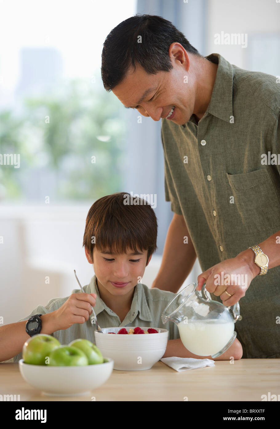 Lächelnden Vater Gießen Milch auf Sohnes Getreide Stockfoto