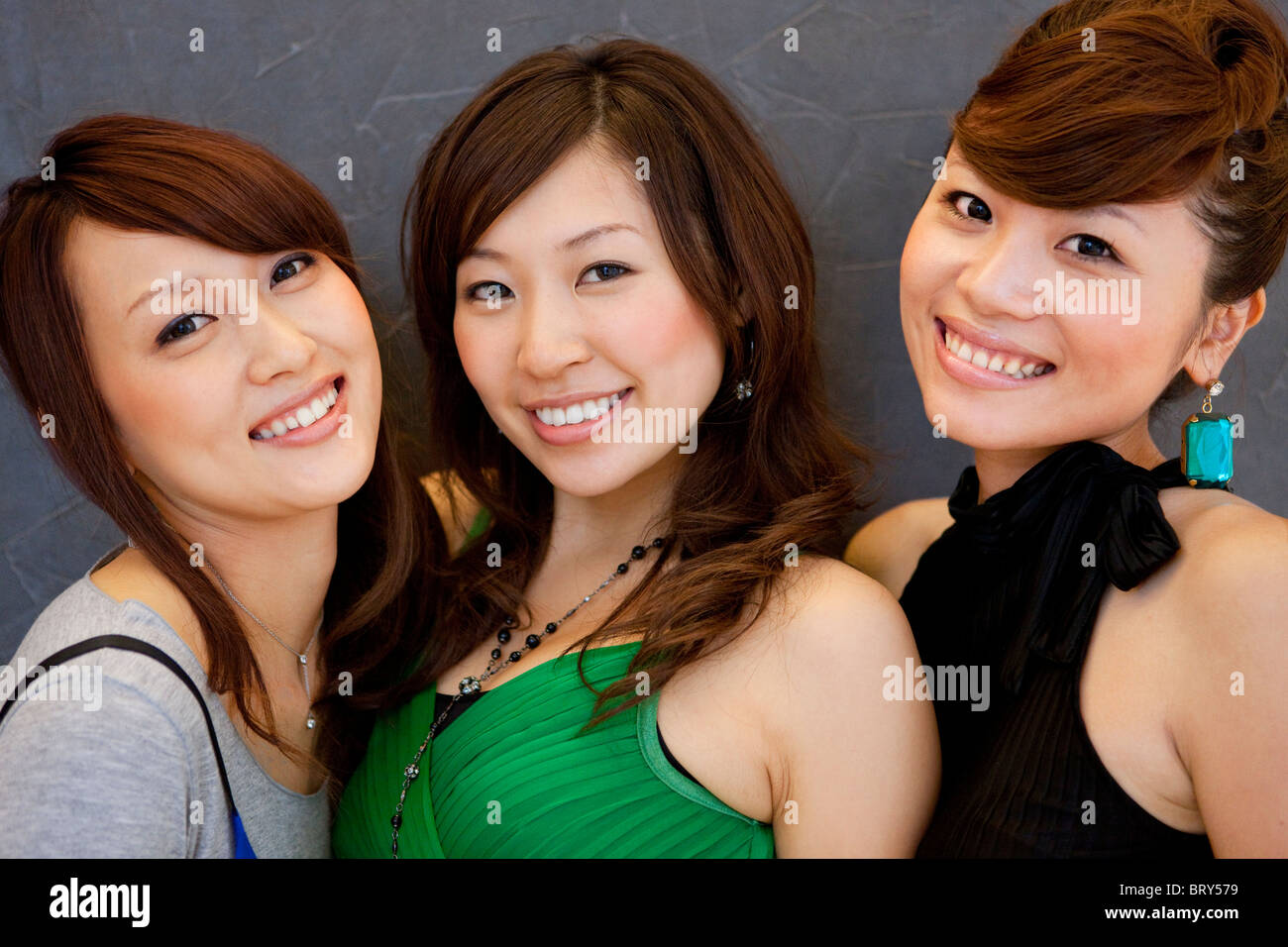 Porträt dreier junger Frauen, lächelnd und mit Blick auf die Kamera, schwarzer Hintergrund Stockfoto