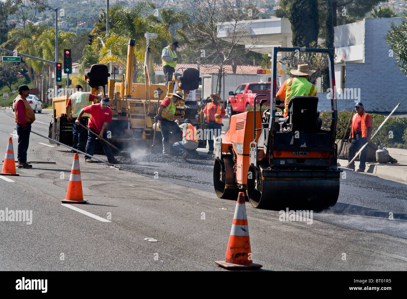 Mit einer Dampfwalze, verbreiten Hispanic Arbeiter tragen Hochsicht Sicherheitsshirts und Westen frischen heißen Brei in einer Straße Stockfoto