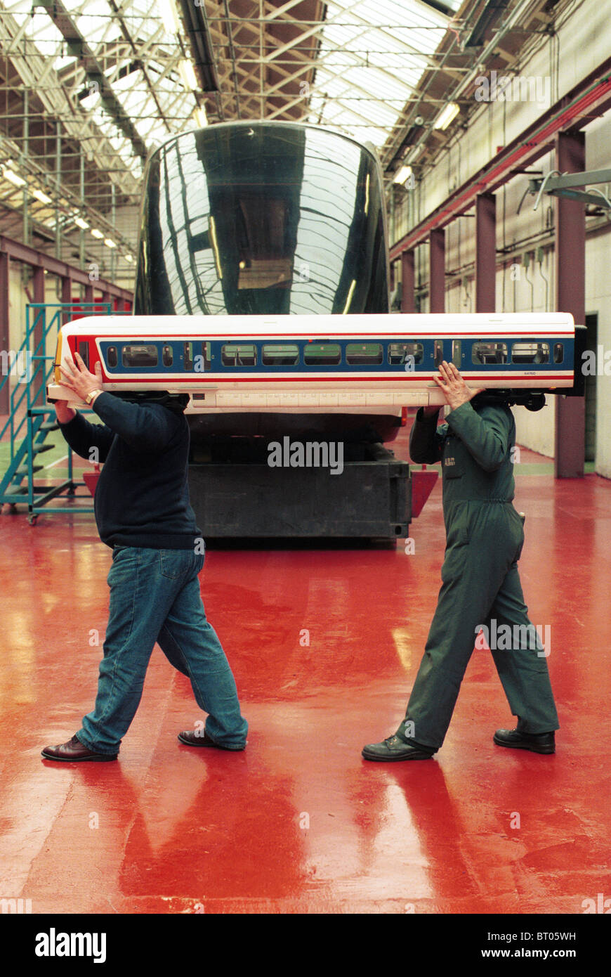 Arbeiter tragen eine maßstabgetreues Modell Zug vorbei ein full-Size-Zug am Derby ABB trainieren Werke im Vereinigten Königreich. Stockfoto