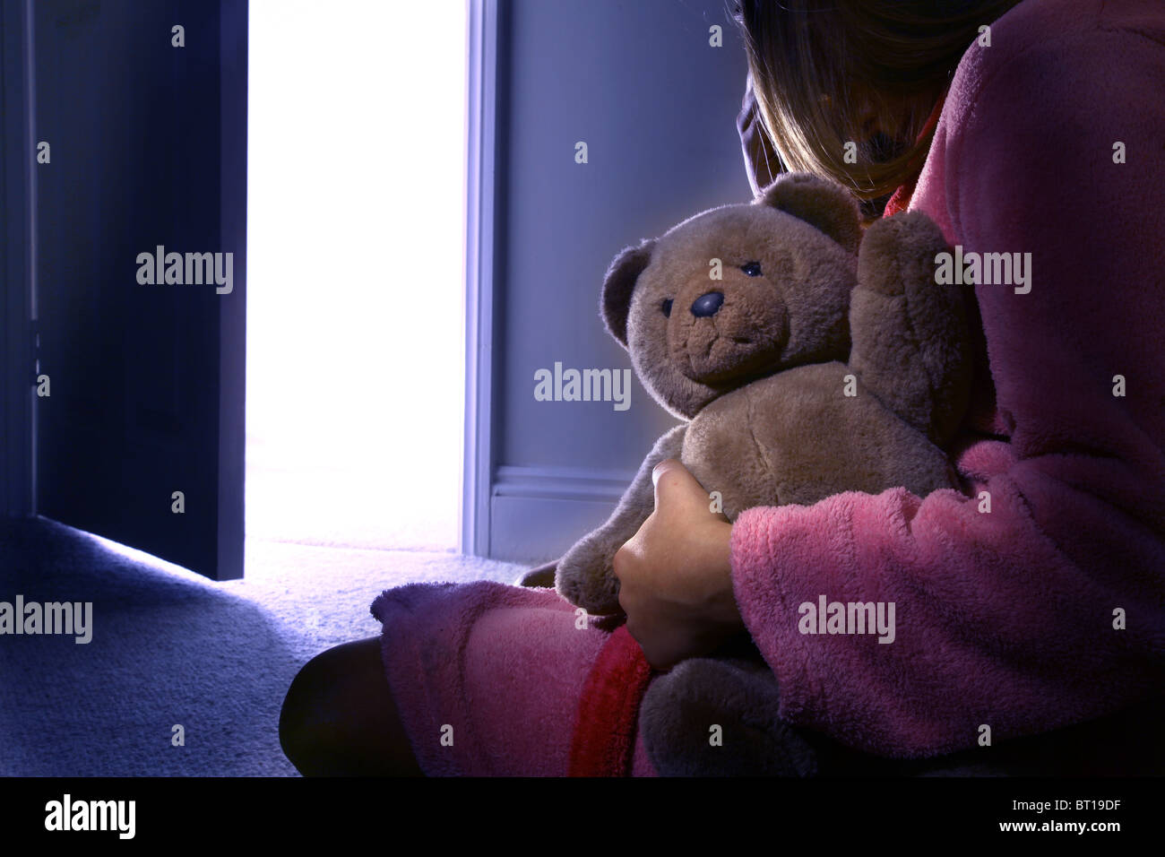 Kleines Mädchen allein in einem dunklen Raum mit einem Teddybär, Rückansicht. 1 Stockfoto