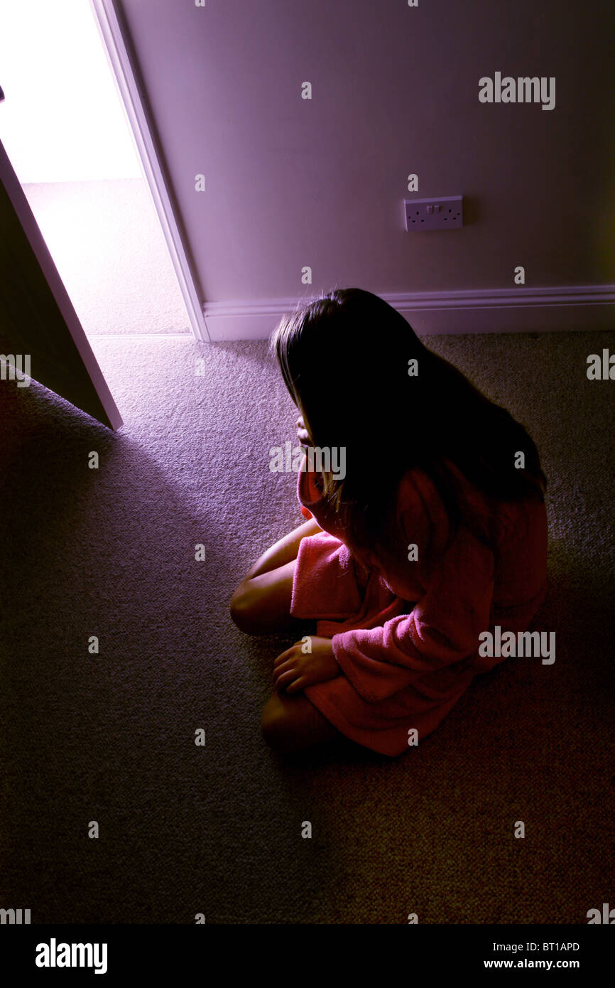 Junges Mädchen am Boden von einem dunklen Raumlicht strömt in den Raum Stockfoto