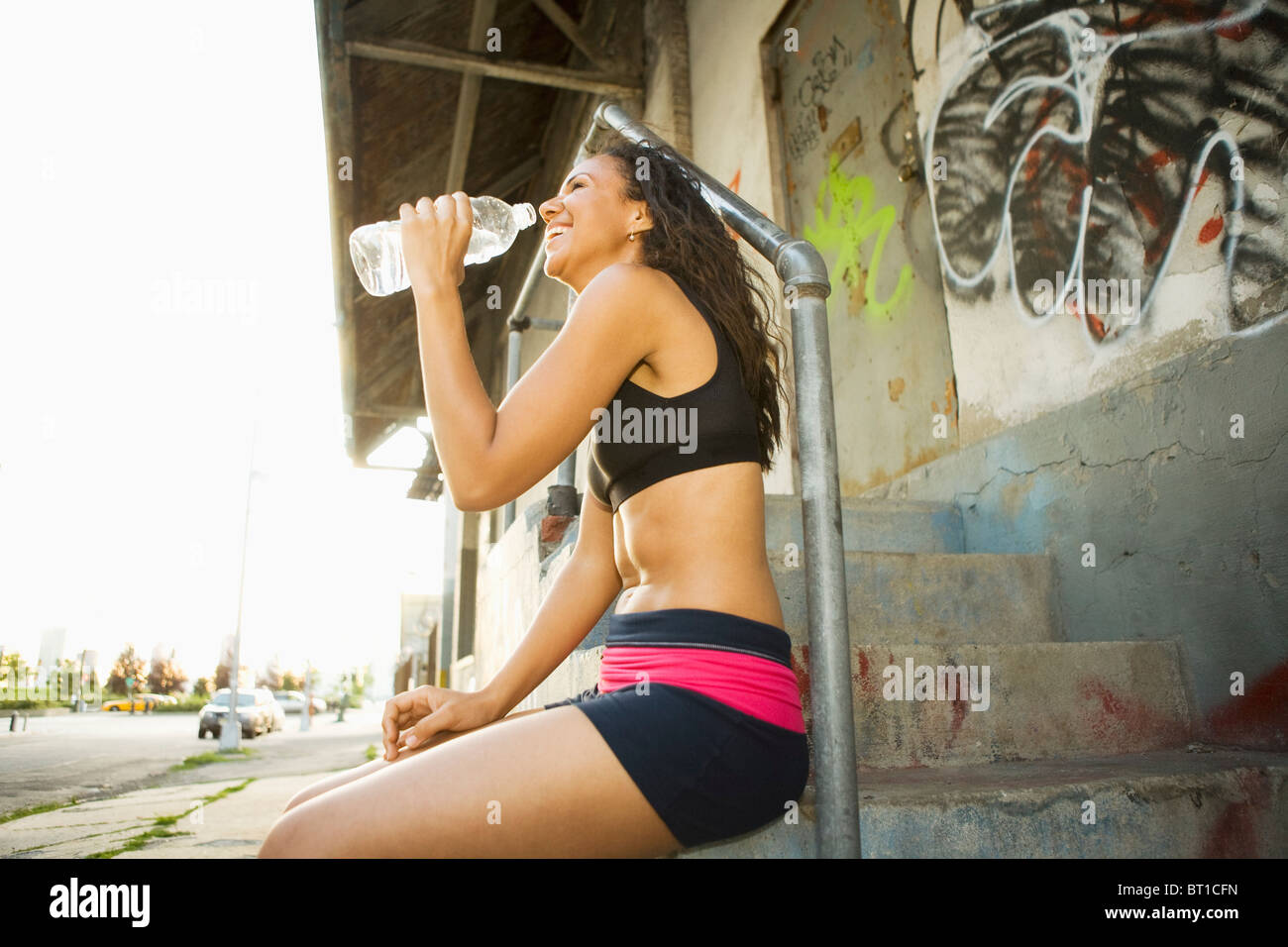 Lächelnde Hispanic Frau Trinkwasser auf städtischen Treppe Stockfoto