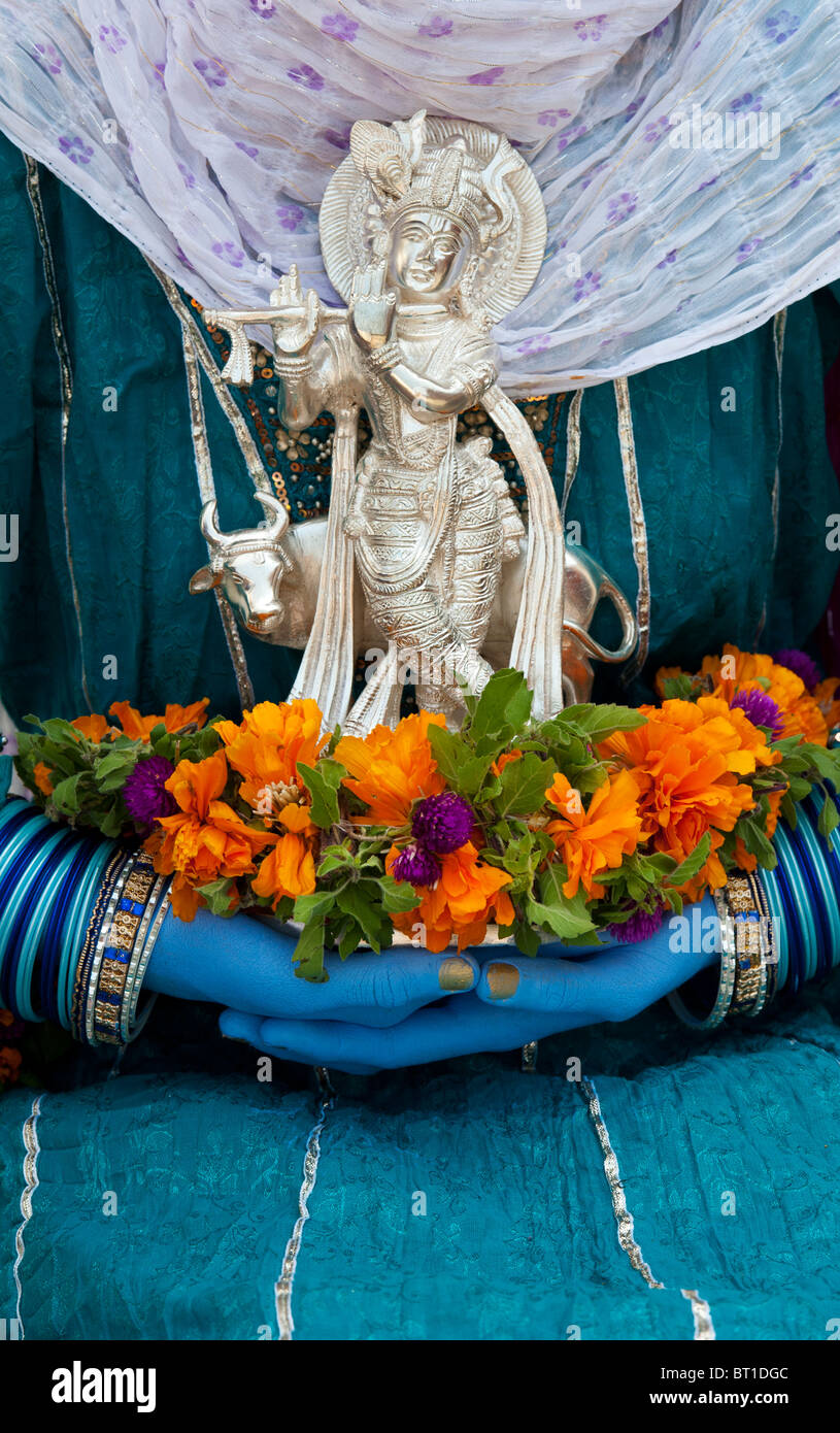 Indische Mädchen, dass eine Silber Krishna Statue und Blumen mit blauen Händen. Indien Stockfoto