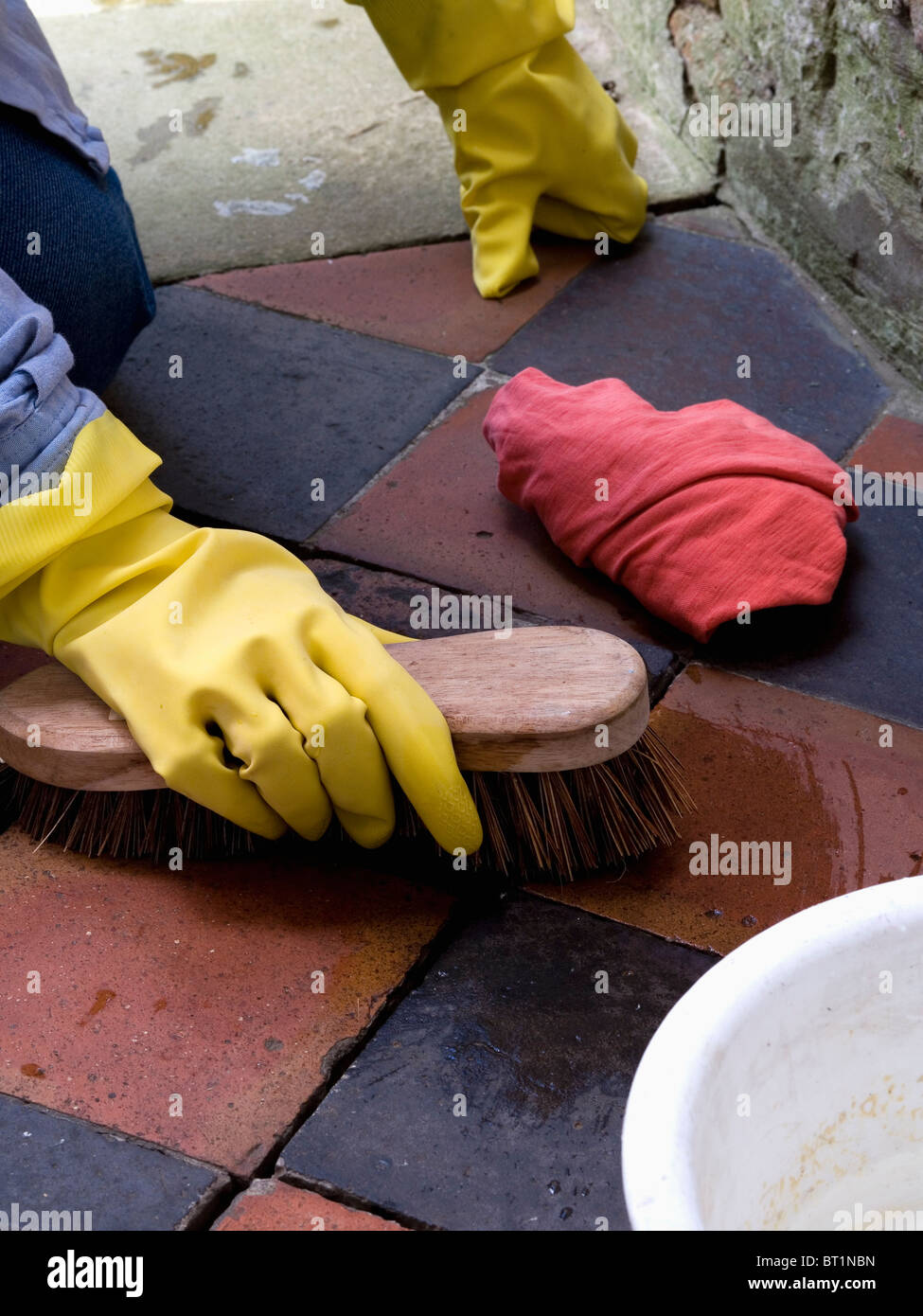 Nahaufnahme der Hand im gelben Gummihandschuh mit Drahtbürste reinigen alten Steinbruch gekachelten Fußboden Stockfoto