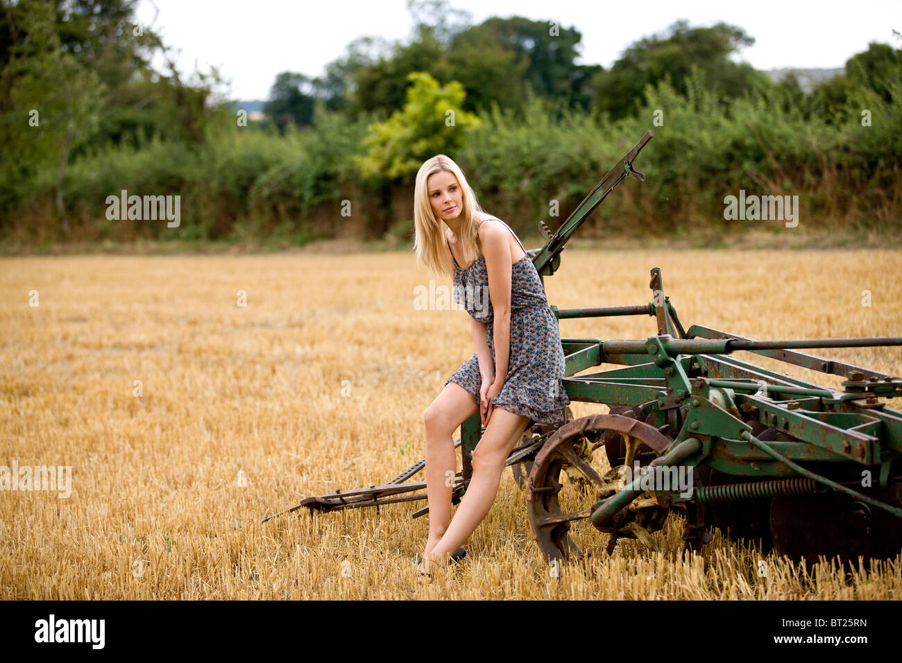 Eine Frau sitzt auf Landmaschinen in einem abgeernteten Weizenfeld Stockfoto