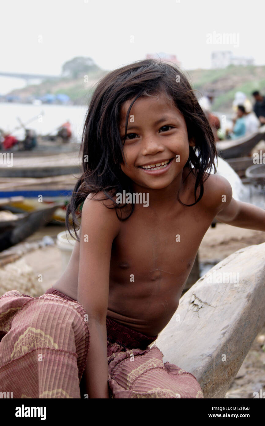 Eine junge Asiatin, die in Armut lebenden sitzt auf einem Holzboot lächelnd am Ufer des Mekong-Flusses im ländlichen Kambodscha. Stockfoto