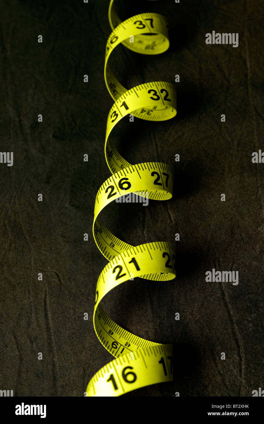 Ein aufgerollter gelben Maßband vor einem dunklen Hintergrund Stockfoto
