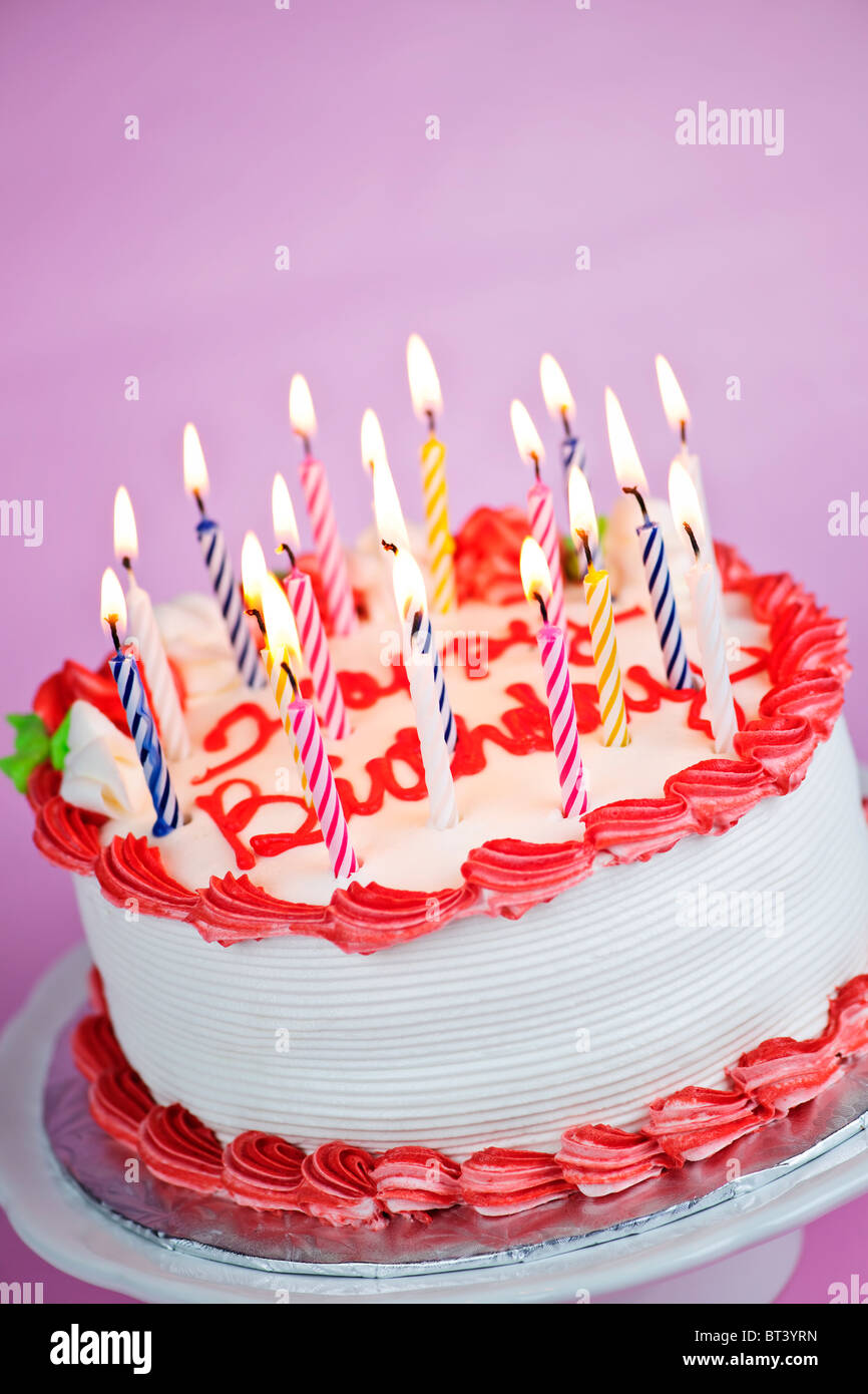 Geburtstagstorte mit brennenden Kerzen auf einem Teller auf rosa Hintergrund Stockfoto