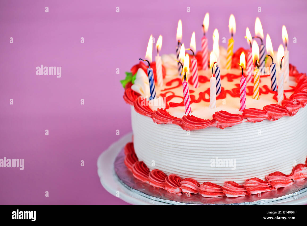 Geburtstagstorte mit brennenden Kerzen auf einem Teller auf rosa Hintergrund Stockfoto