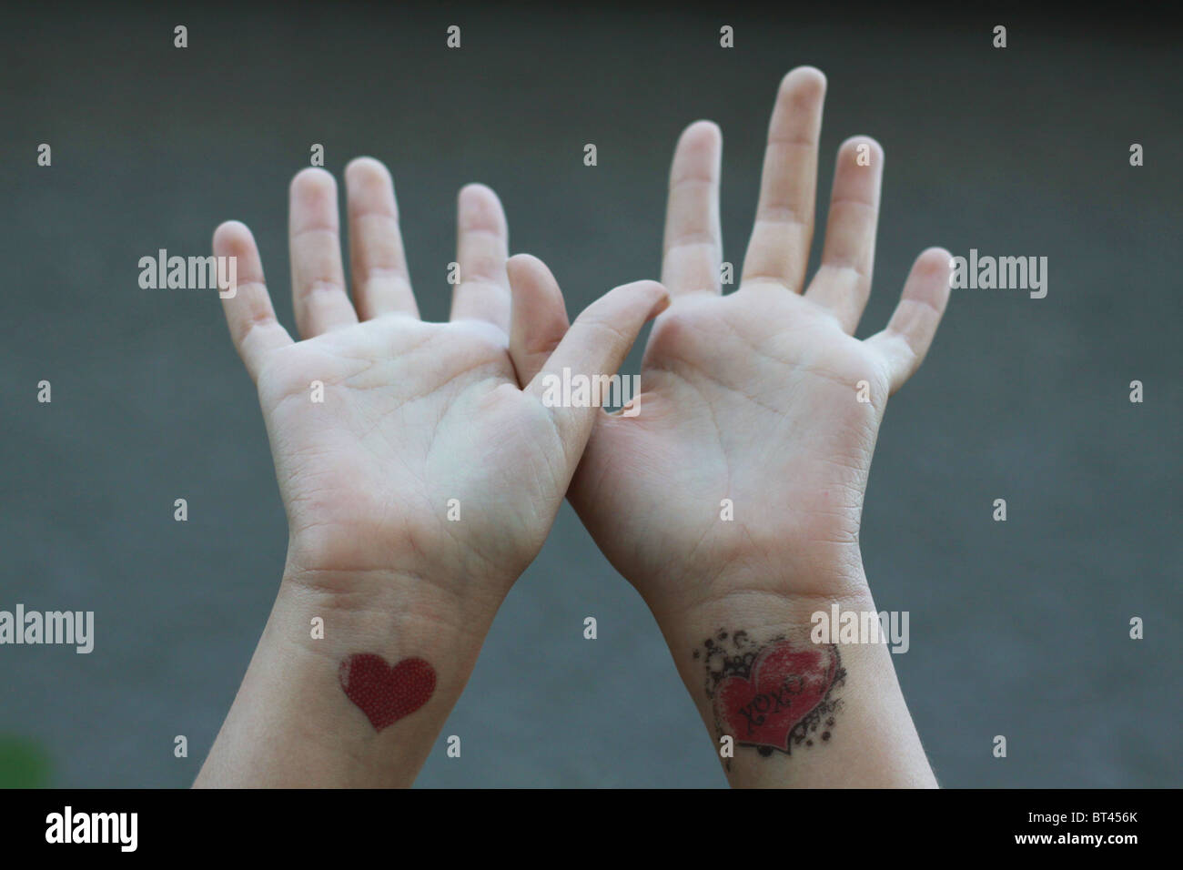 Eine Nahaufnahme von Handzeichen zum Himmel, mit fading Herzen Tattoos an jedem Handgelenk. Stockfoto