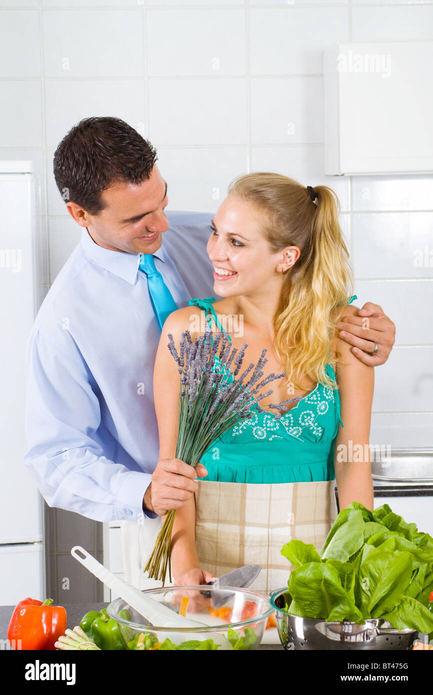 junger Mann kommt nach Hause mit Blume zu seiner fleißigen Frau geben Stockfoto