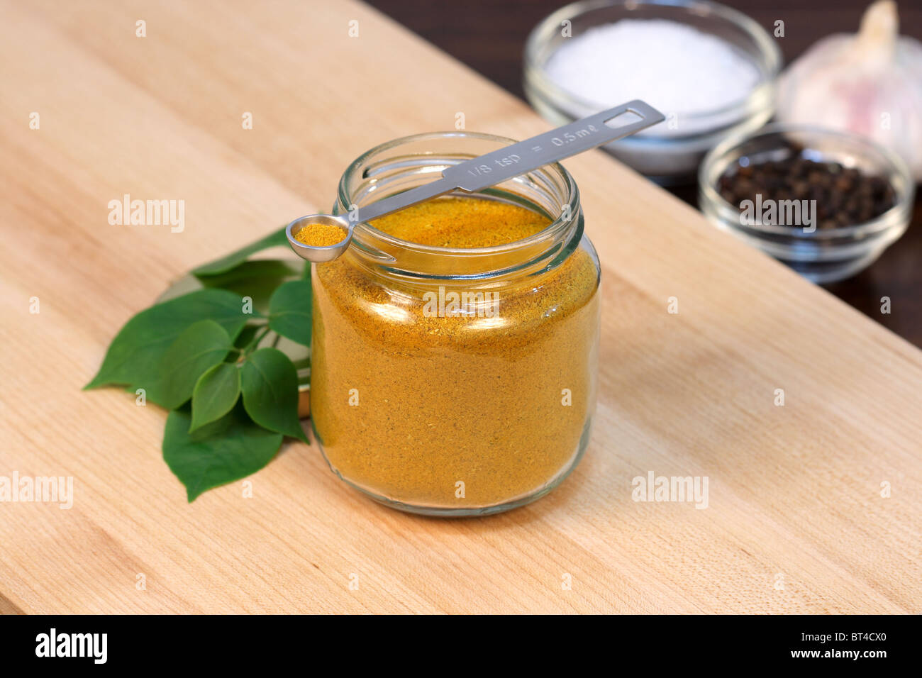 Curry-Pulver auf feine Holz Schneidebrett mit grobem Salz, Knoblauch, Pfeffer und Messlöffel Stockfoto