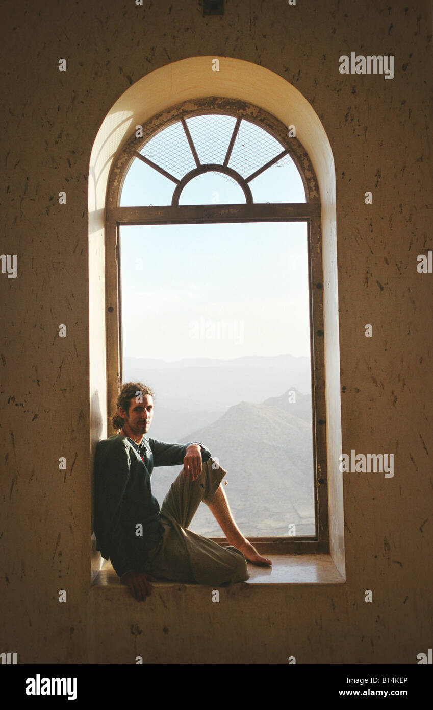 Männlichen Reisenden sitzt im Fenster in der geistlichen Betrachtung mit Blick über die Berge von der Monsun-Palast in Udaipur, Indien. Stockfoto