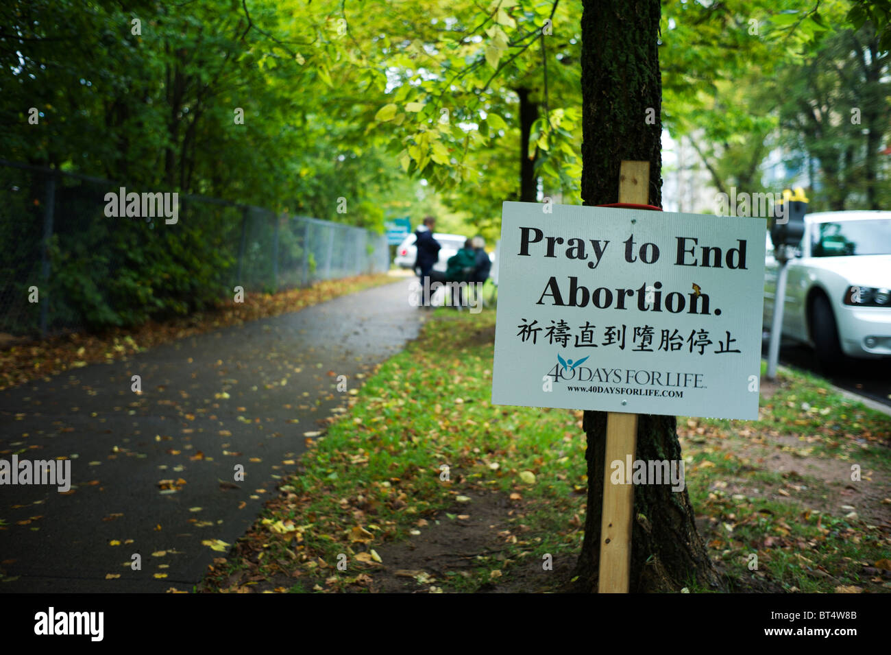 Anti-Abtreibungs-Zeichen und Demonstranten auf Bäumen gesäumten Bürgersteig. Stockfoto