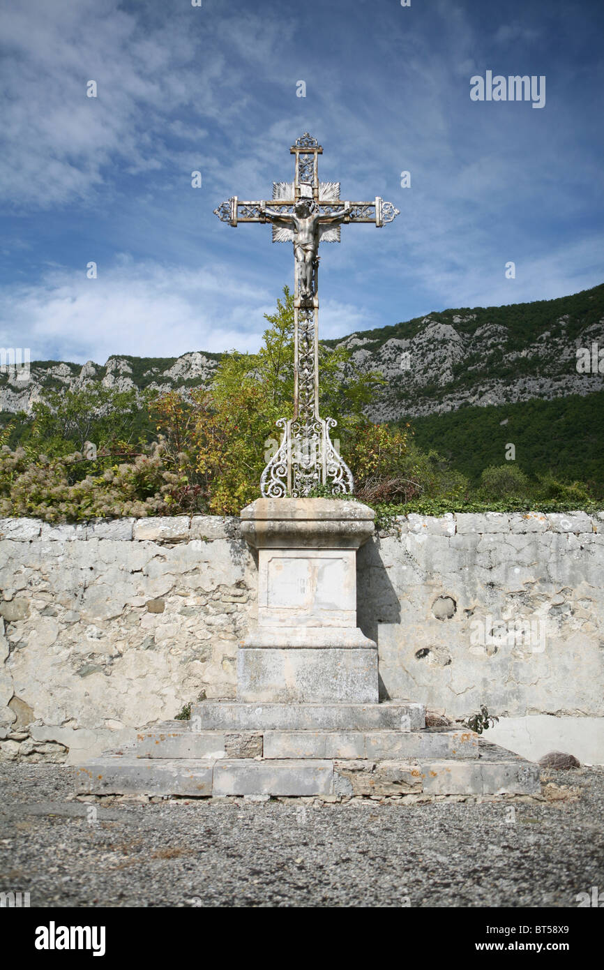 Ein großes Metallkreuz auf einem Steinsockel auf einem ländlichen Bergdorffriedhof in Saou, Drôme, Frankreich. Stockfoto