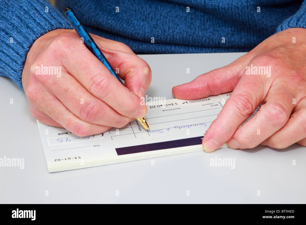 Nahaufnahme einer reifen Frau einen Scheck (Scheck) in einem Scheckbuch schreibt, eine Rechnung zu bezahlen. England, UK, Großbritannien. Stockfoto