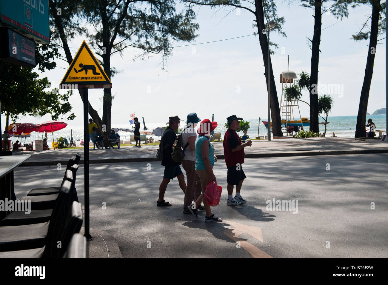 Touristen, die beim Überqueren der Straße neben einem betrunken Menschen Kreuzung Schild von Pa Tong Beach, Phuket, Thailand Stockfoto