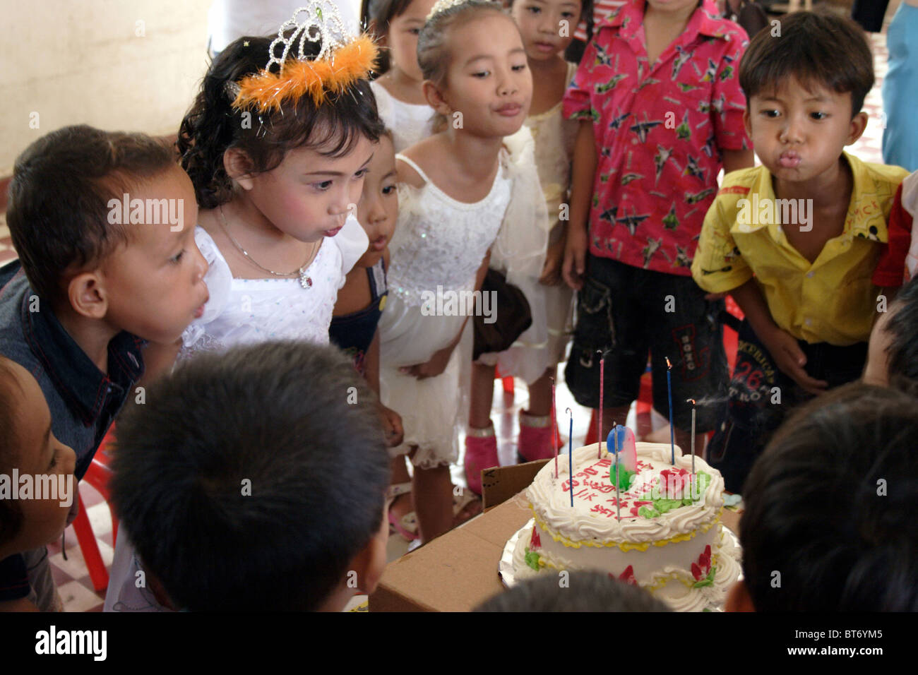 Eine 6-jährige Asiatin bläst 6 Kerzen auf einem Geburtstagskuchen mit Freunden glückliche Schulkinder in Kambodscha. Stockfoto